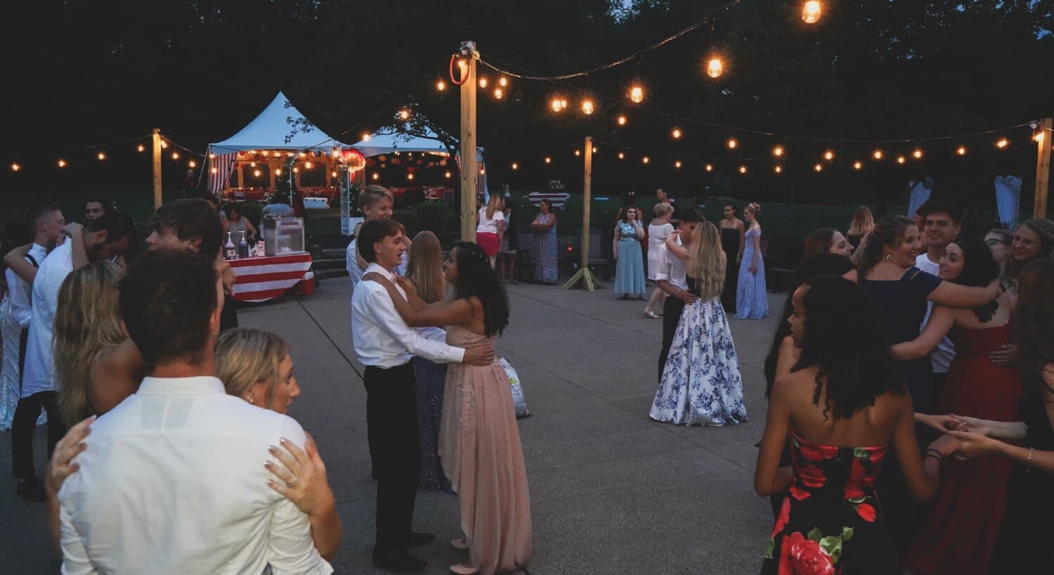 People dancing on an outdoor patio with string lights and an event tent set up in the background