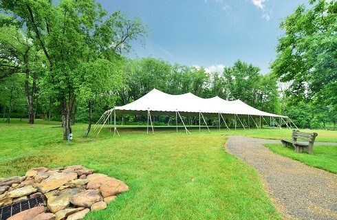 Large white outdoor event tent set up on a lawn surrounded by trees and two pathways