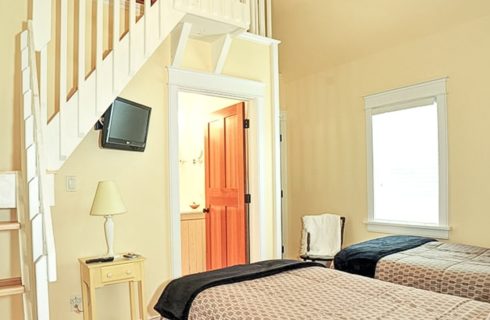 Two twin beds in a bedroom with stairs to a loft above and doorway into a bathroom