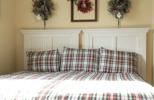 Two twin beds in a plaid quilt together as a king bed with light sconces and wreaths on the wall above