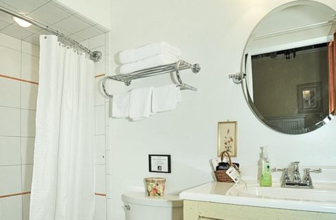 Bathroom with single vanity sink, stand up shower, round mirror and rack with white towels