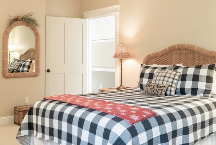 Bright bedroom with queen bed featuring a black and white buffalo check quilt and wicker headboard