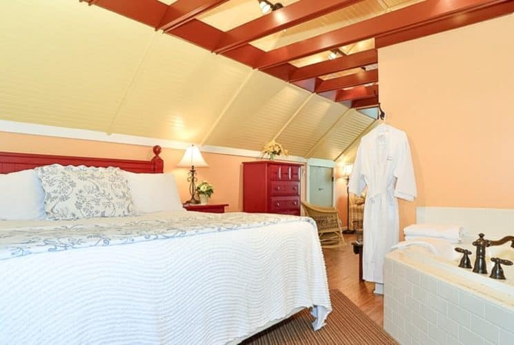King sized bed with red headboard in loft bedroom with large jacuzzi tub, dresser and open wood beam ceiling