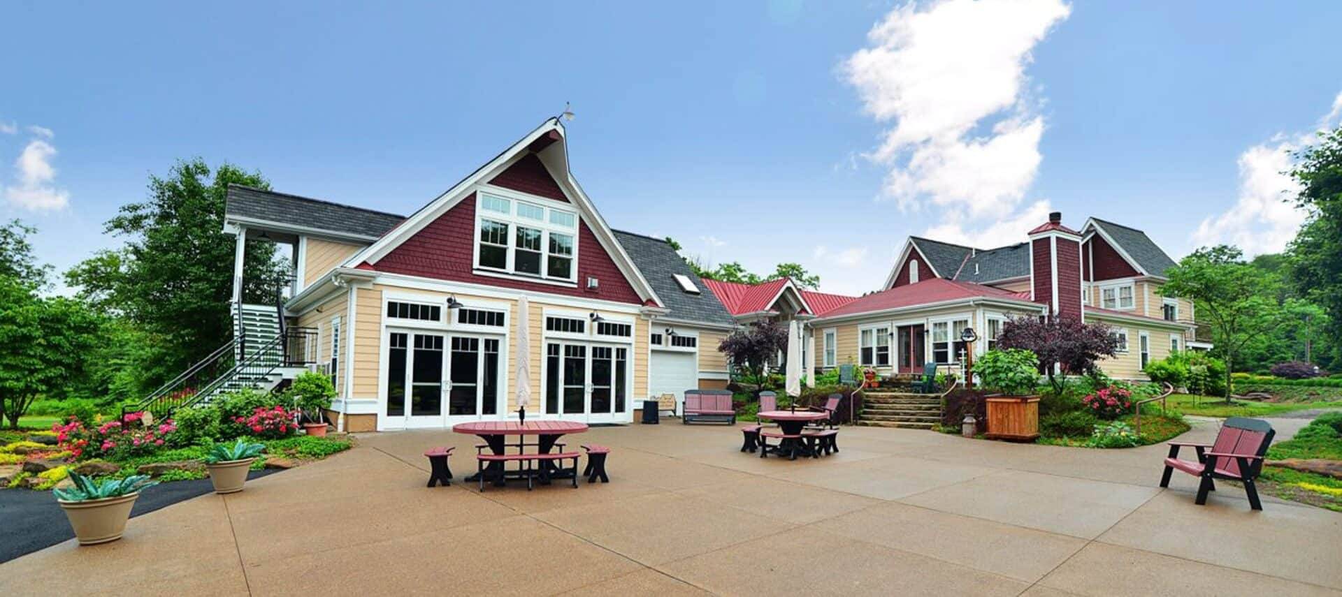 Expansive patio outside of a large home with lush landscaping, tables, chairs and benches