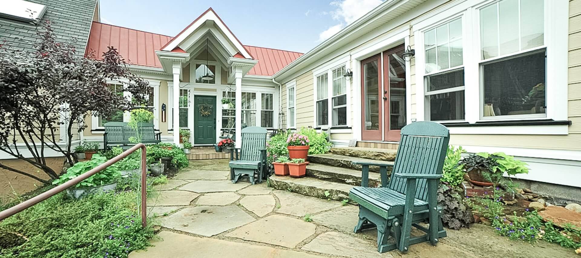 Stone patio in front of a home with a stairway up to a set of doors and large portico over a front door