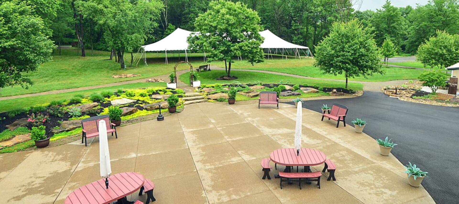 A large outdoor patio with tables, chairs, benches and white outdoor tent on a lawn in the background